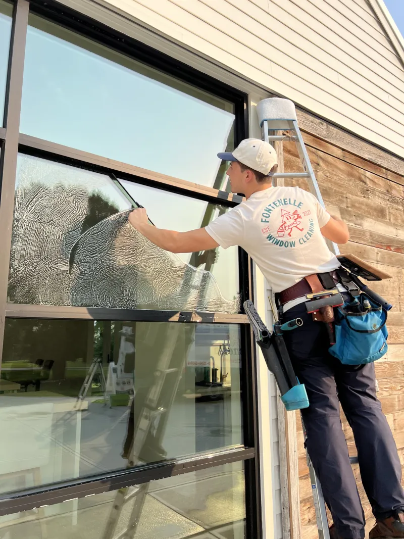 Fontenelle technician cleaning a second-story window from a ladder in Omaha